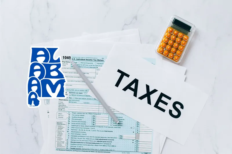 A capital gains calculator sits next to tax forms, a paper with the word 'TAXES', and an Alabama state logo on a white marble surface.