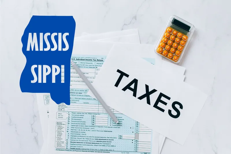 A capital gains calculator sits next to tax forms, a paper with the word 'TAXES', and an Mississippi state logo on a white marble surface.