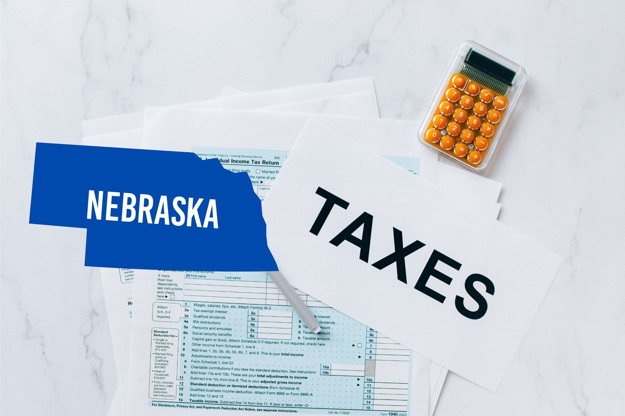 A capital gains calculator sits next to tax forms, a paper with the word 'TAXES', and an Nebraska state logo on a white marble surface.
