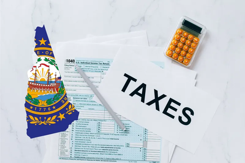 A capital gains calculator sits next to tax forms, a paper with the word 'TAXES', and an New Hampshire state logo on a white marble surface.