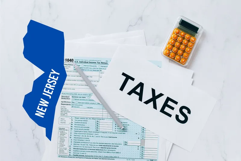 A capital gains calculator sits next to tax forms, a paper with the word 'TAXES', and an New Jersey state logo on a white marble surface.