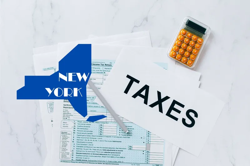 A capital gains calculator sits next to tax forms, a paper with the word 'TAXES', and an New York state logo on a white marble surface.