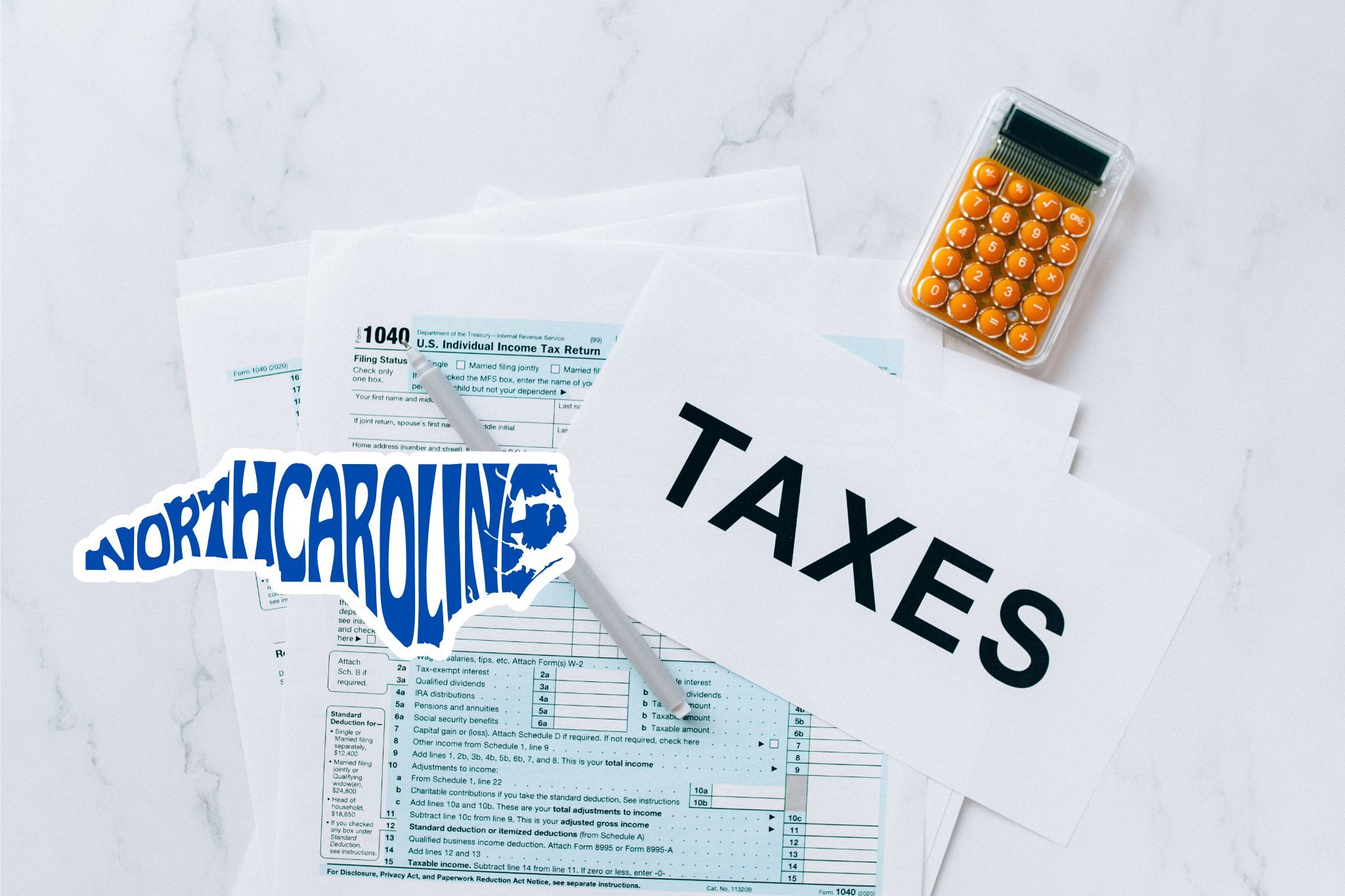 A capital gains calculator sits next to tax forms, a paper with the word 'TAXES', and an North Carolina state logo on a white marble surface.