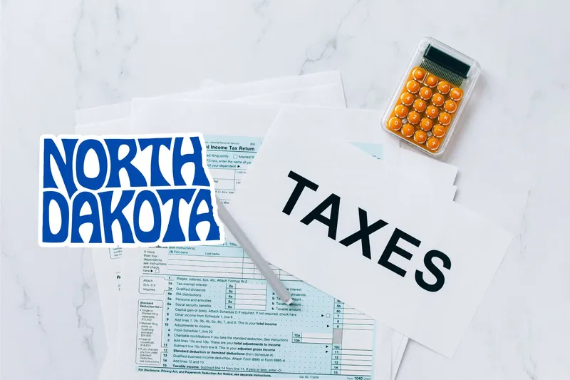 A capital gains calculator sits next to tax forms, a paper with the word 'TAXES', and an North Dakota state logo on a white marble surface.