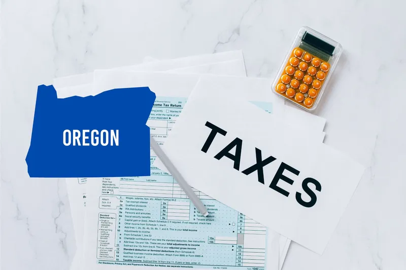 A capital gains calculator sits next to tax forms, a paper with the word 'TAXES', and an Oregon state logo on a white marble surface.