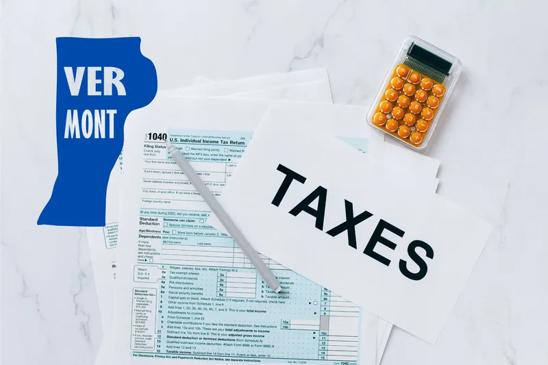 A capital gains calculator sits next to tax forms, a paper with the word 'TAXES', and an Vermont state logo on a white marble surface.