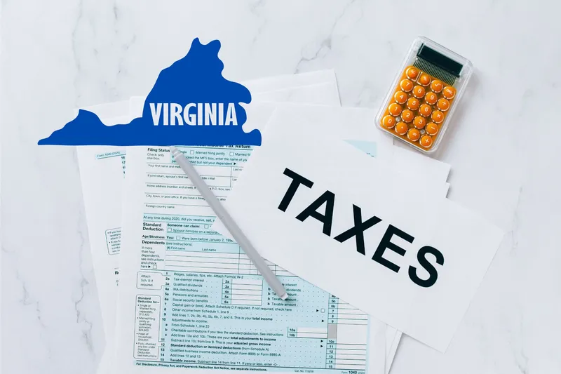 A capital gains calculator sits next to tax forms, a paper with the word 'TAXES', and an Virginia state logo on a white marble surface.