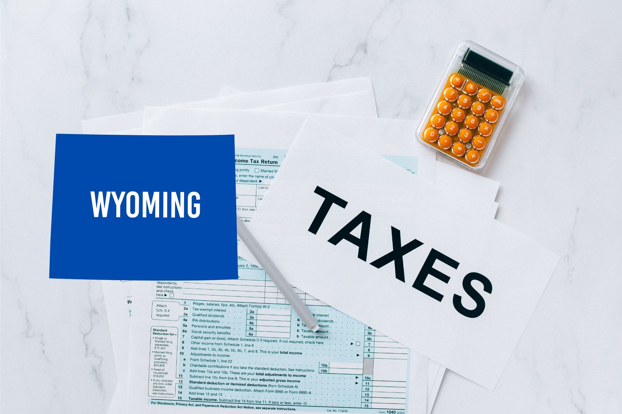 A capital gains calculator sits next to tax forms, a paper with the word 'TAXES', and an Wyoming state logo on a white marble surface.
