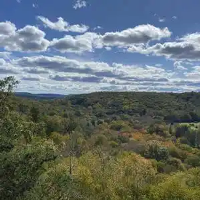 A dense Connecticut forest landscape with rolling hills under a partly cloudy sky, viewed from an elevated vantage point.