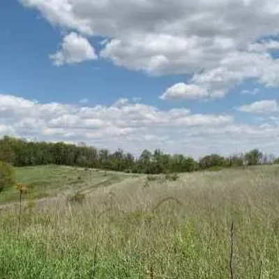 A grassy field stretches beneath a sky filled with scattered clouds. Trees line the horizon, and a few trees are visible in the background, evoking the peaceful, rural landscapes of Pennsylvania.