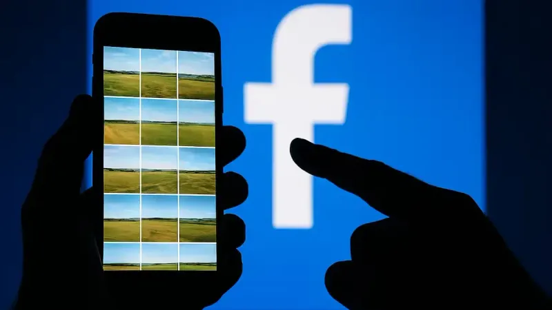 Hand holding smartphone in front of Facebook logo