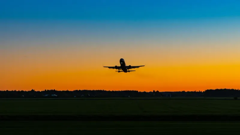 Selling out-of-state property: Airplane silhouette flies low over agricultural land during a vibrant sunset.